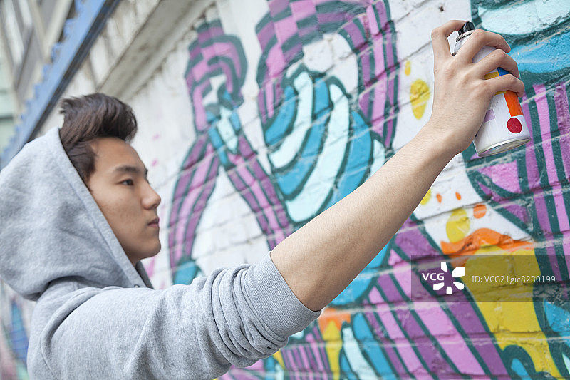 手持喷漆罐在墙上喷漆的专注青年图片素材