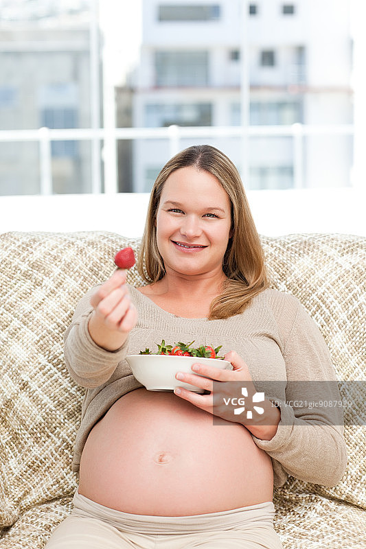 准妈妈坐在家里的沙发上，手里拿着一碗草莓图片素材