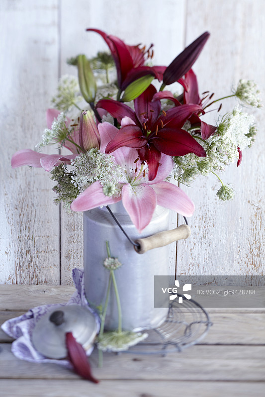 旧牛奶罐里的百合花和野胡萝卜花束图片素材