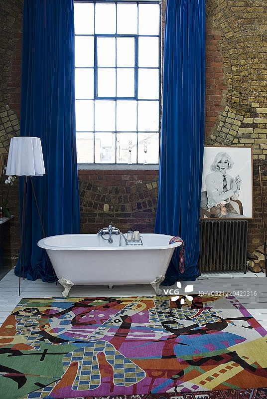 阁楼浴室：彩色地毯和蓝色窗帘前的独立式复古浴缸图片素材