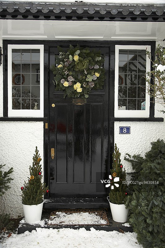 英式乡村住宅的前门，带有基督降临节花环和装饰圣诞节的盆栽针叶树图片素材