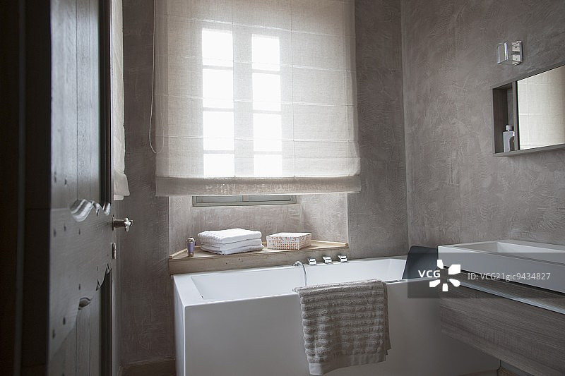 设计师浴室：透过敞开的门，可以看到窗户下的浴缸，以及墙上现代的槽式洗脸盆图片素材