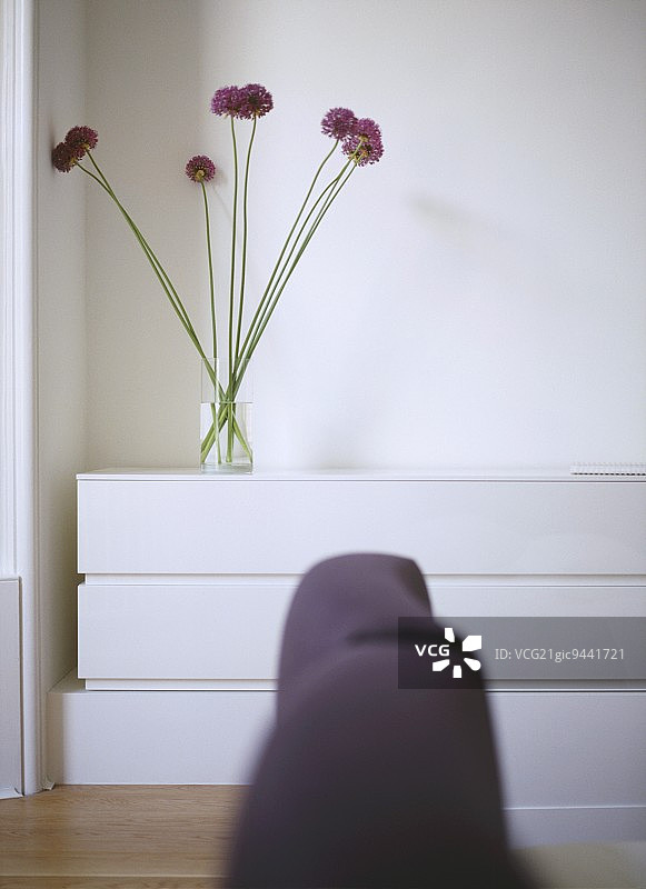 现代白色卧室细节：软包床头板和玻璃花瓶中的葱属植物图片素材