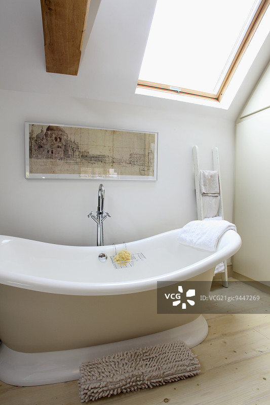 白色浴室中的柔和米色和木色调，倾斜天窗下的独立浴缸图片素材