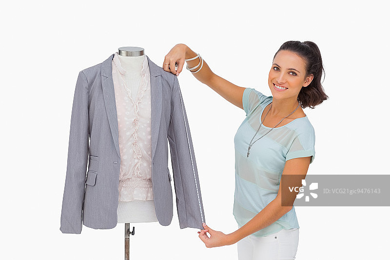 时装设计师在人体模型上测量西装外套的袖子，在白色背景上微笑图片素材