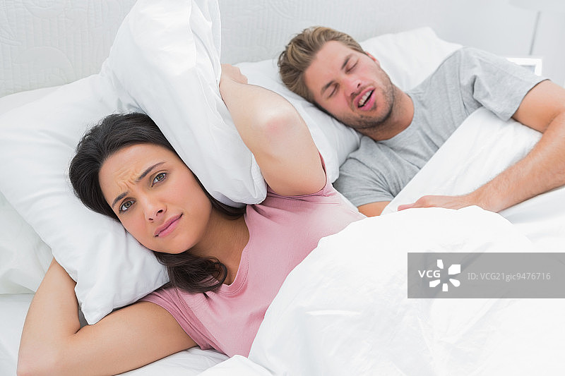 女子用枕头捂住耳朵，丈夫在一旁打鼾图片素材