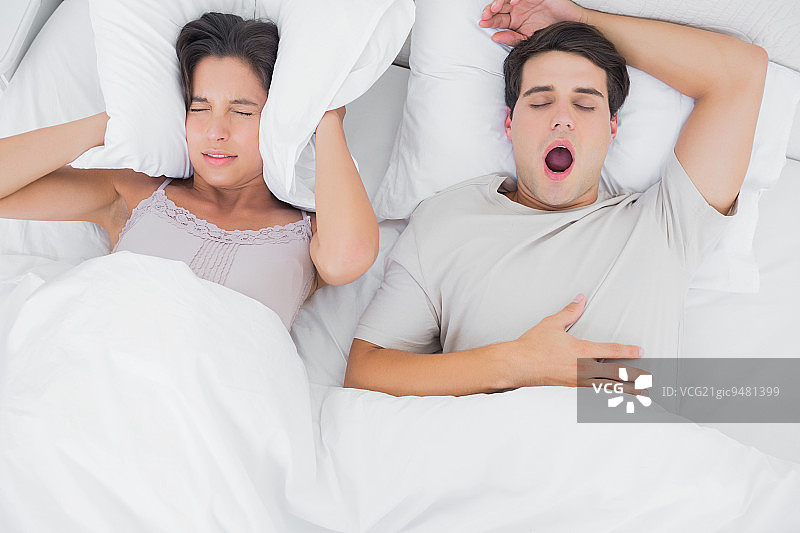 女人用枕头捂住耳朵，而她的伴侣在她旁边打鼾图片素材