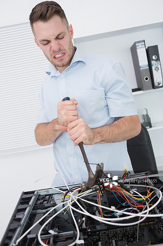 沮丧的年轻男子在办公室用锤子从CPU上拔出电线图片素材