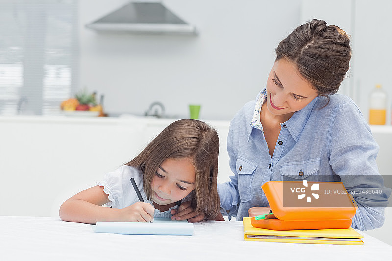 母亲看着女儿在厨房里画画图片素材