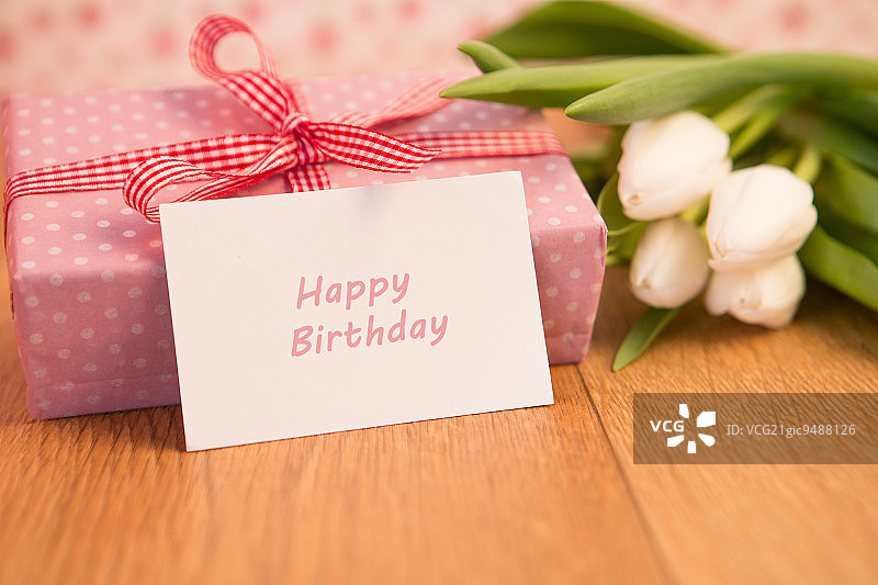 木桌上白色郁金香和生日贺卡旁的粉色包装礼物图片素材