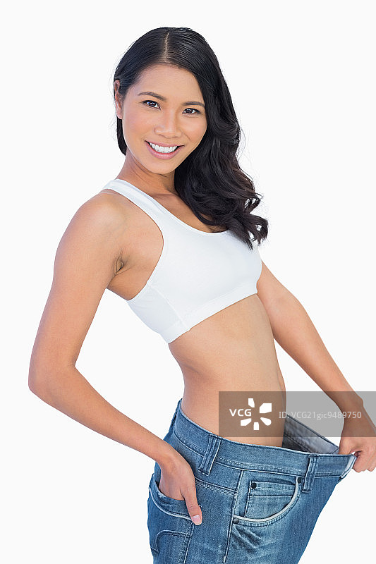 快乐的女人在白色背景下拿着她太大的裤子图片素材