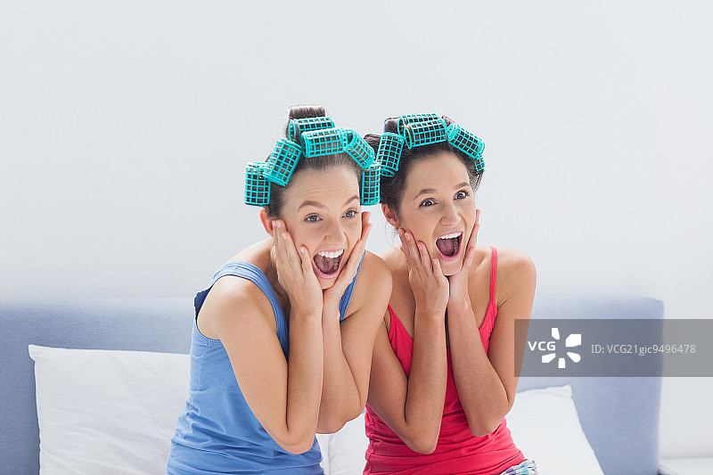 朋友们在睡衣派对上，坐在床上，戴着发卷，尖叫着图片素材