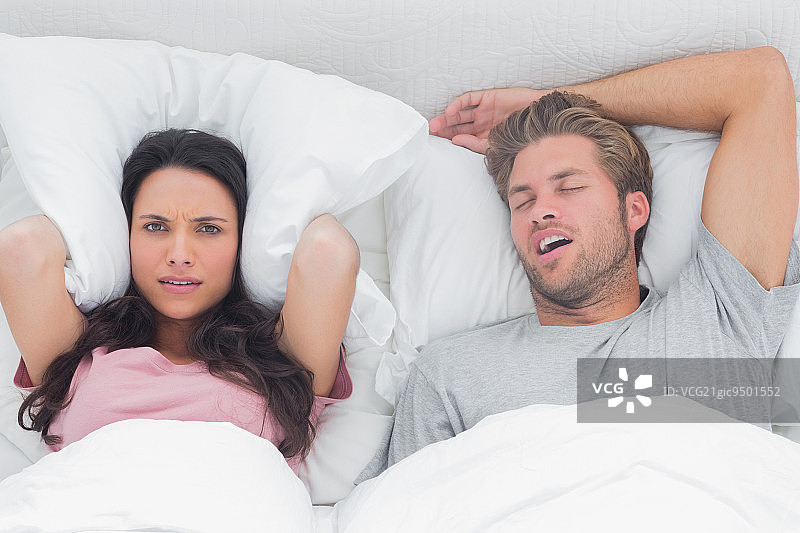 女人用枕头捂住耳朵，因为她被丈夫的鼾声吵醒图片素材