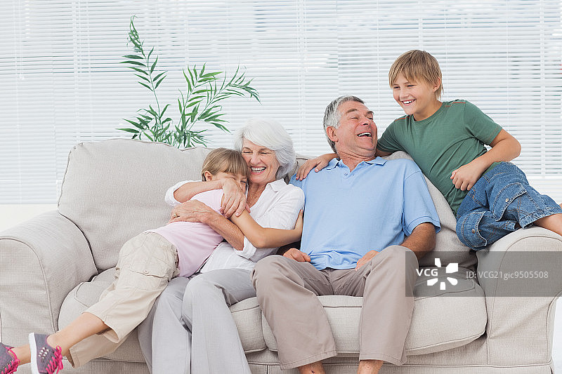 笑容满面的孙子孙女拥抱坐在沙发上的祖父母图片素材