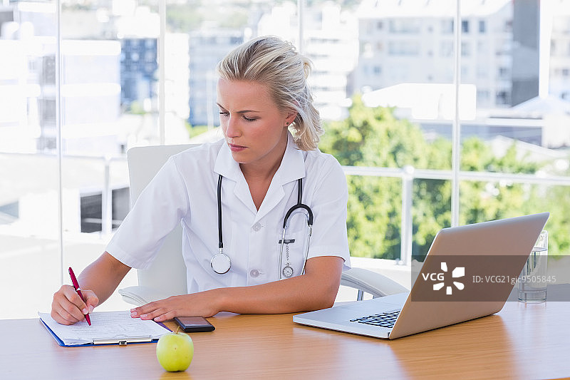 办公室里在办公桌上用笔记本电脑写作的金发护士图片素材