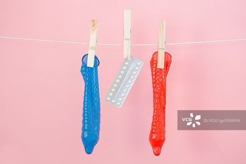 粉色背景上，挂在绳子上的避孕药和避孕套图片素材