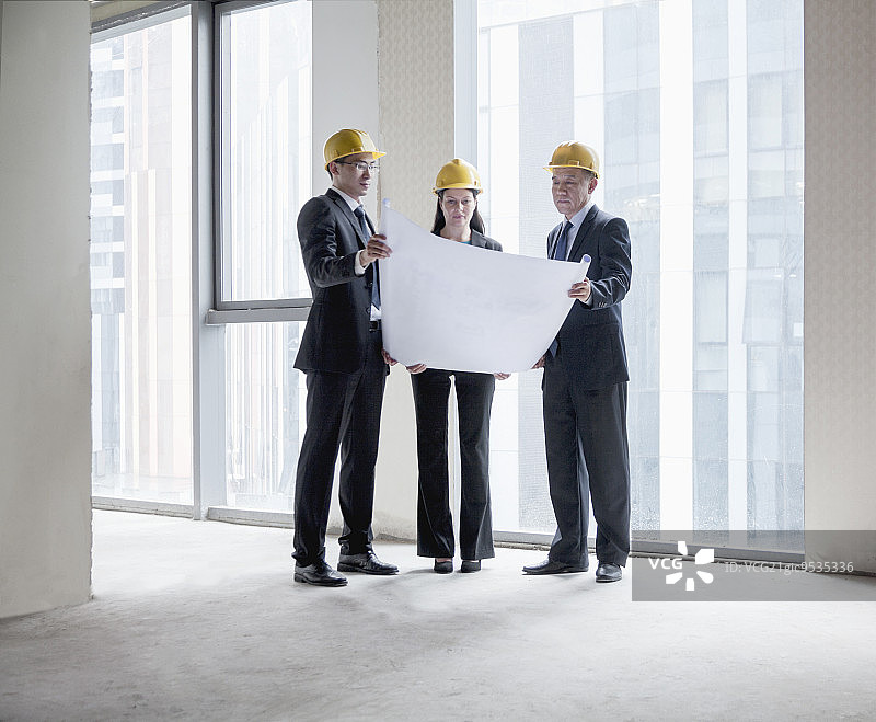 三位戴着安全帽的建筑师在办公楼里检查蓝图图片素材