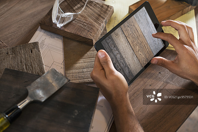 一个年轻男人在工作室里用回收的木材制作家具，并使用平板电脑记录和拍摄作品图片素材