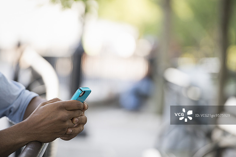 城市之夏：户外的人们，在移动中保持联系，一个男人坐在长椅上使用智能手机图片素材