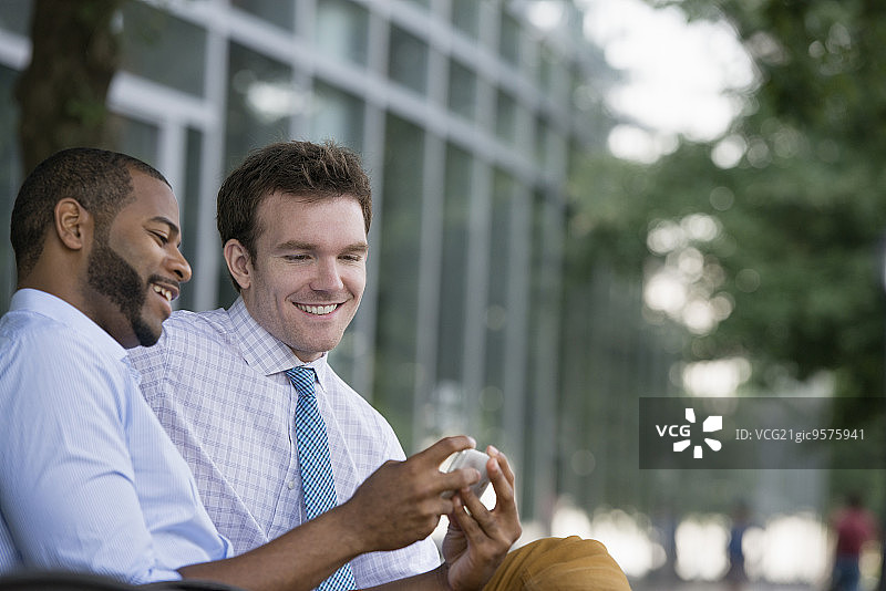 城市之夏：户外商务人士，两位男士坐在长椅上使用智能手机图片素材