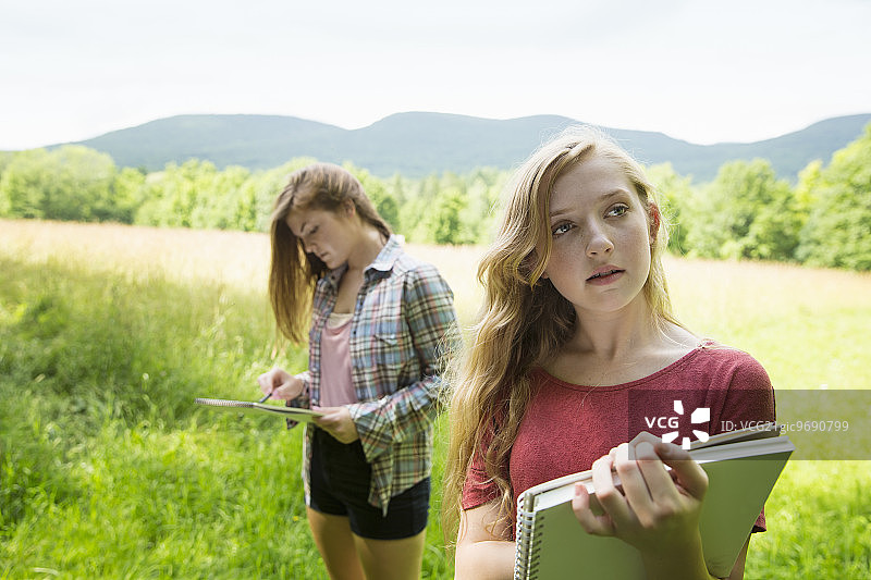 两个年轻女孩坐在草地上，用素描本和铅笔绘画图片素材