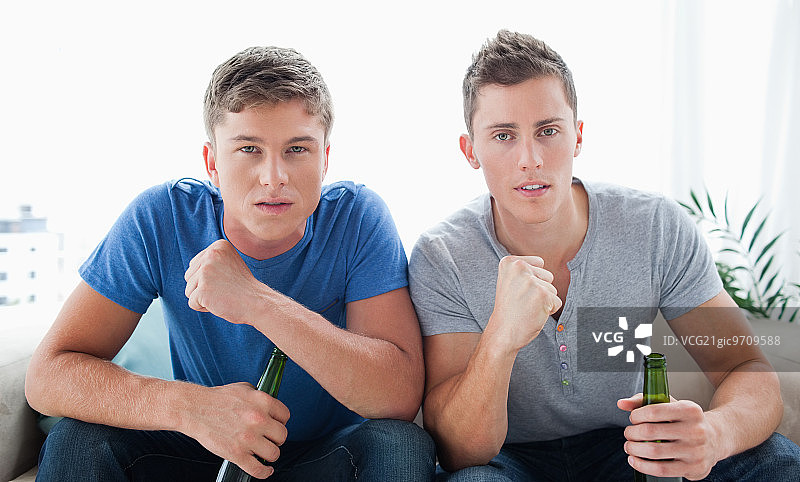 两个男人手持啤酒，看向镜头并挥拳庆祝图片素材