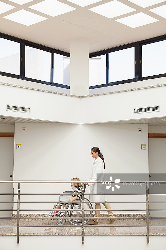 女医生在医院走廊里推着戴着颈托的轮椅儿童图片素材