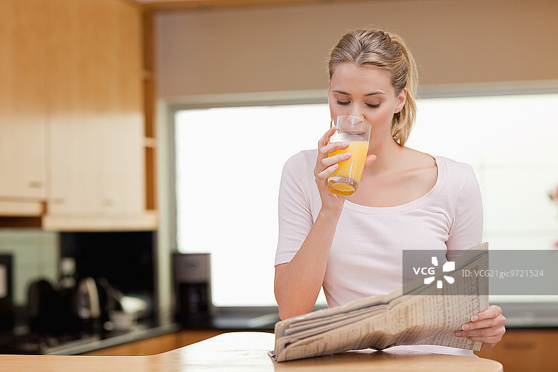 年轻女人在厨房喝橙汁时阅读新闻图片素材