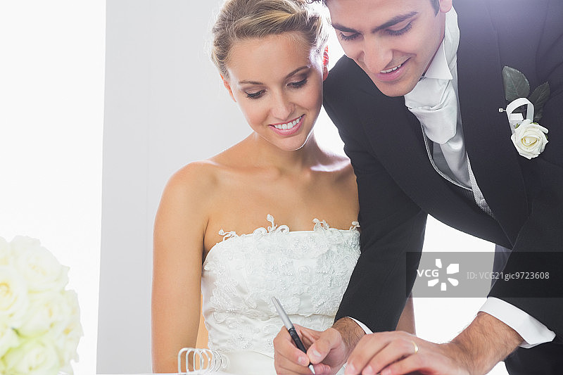 幸福的年轻新郎在妻子身旁签署结婚合同图片素材