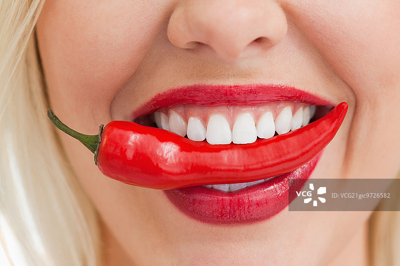 快乐的金发女人用嘴对着白色背景拿着辣椒图片素材