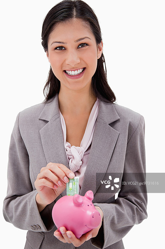 女商人将钱放入白色背景前的存钱罐图片素材