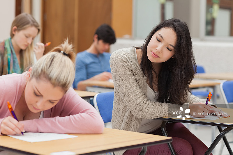 女孩在大学考场考试中抄袭其他学生作业图片素材