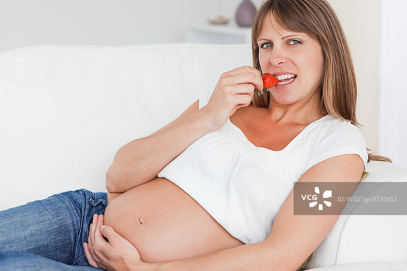 迷人的孕妇躺在沙发上吃草莓图片素材