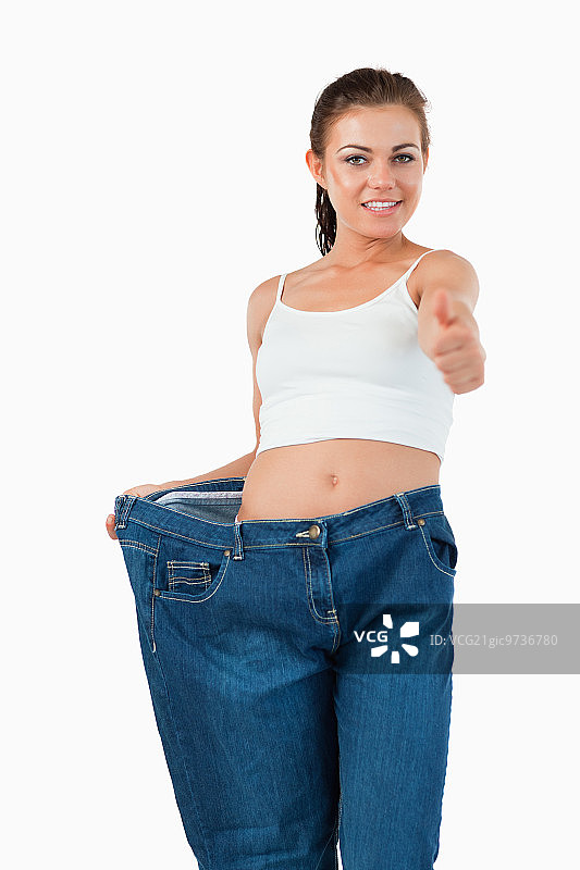 穿着肥大牛仔裤，竖起大拇指的健康女人肖像，白色背景图片素材