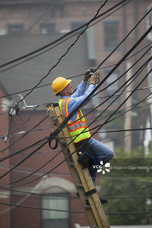 电缆线务员从梯子上评估城市电缆接头图片素材