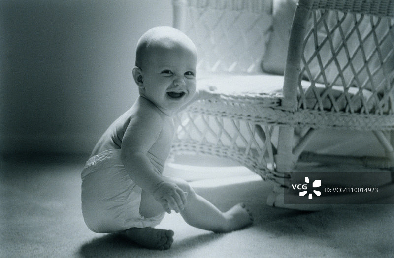 坐在椅子旁，在地板上微笑的婴儿图片素材