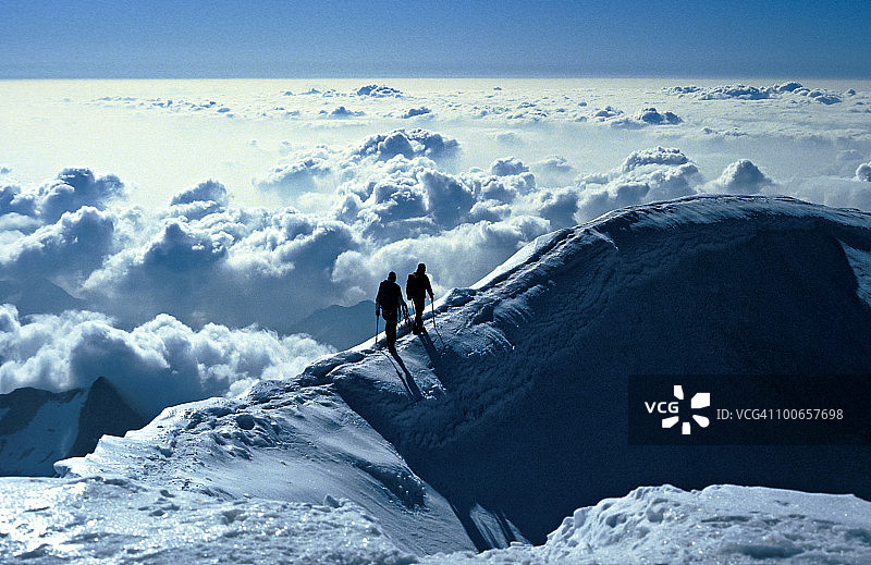 两名登山者在云层之上的冰脊上图片素材