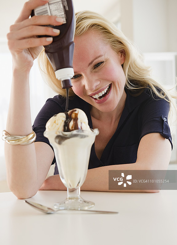年轻女子在冰淇淋上淋巧克力酱图片素材