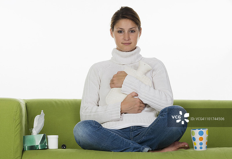 年轻女人坐在沙发上，抱着热水袋图片素材