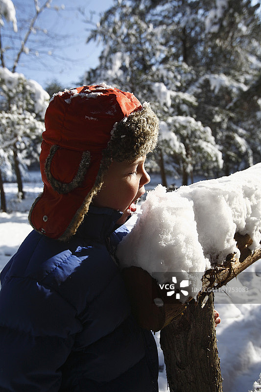 戴皮草帽子的小男孩吃栏杆上的雪图片素材