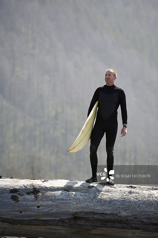 男人站在加州迷失海岸的倒下的树上，拿着冲浪板图片素材