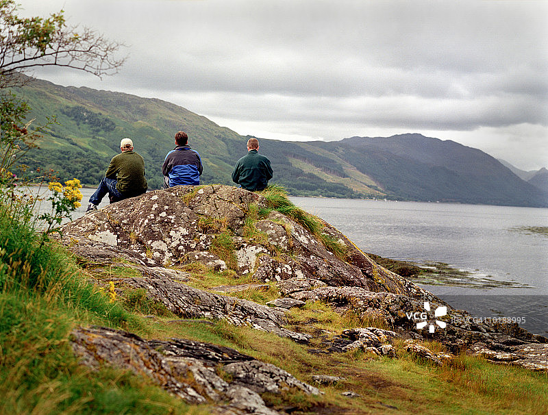 苏格兰高地：三名男子坐在岩石上眺望湖泊图片素材