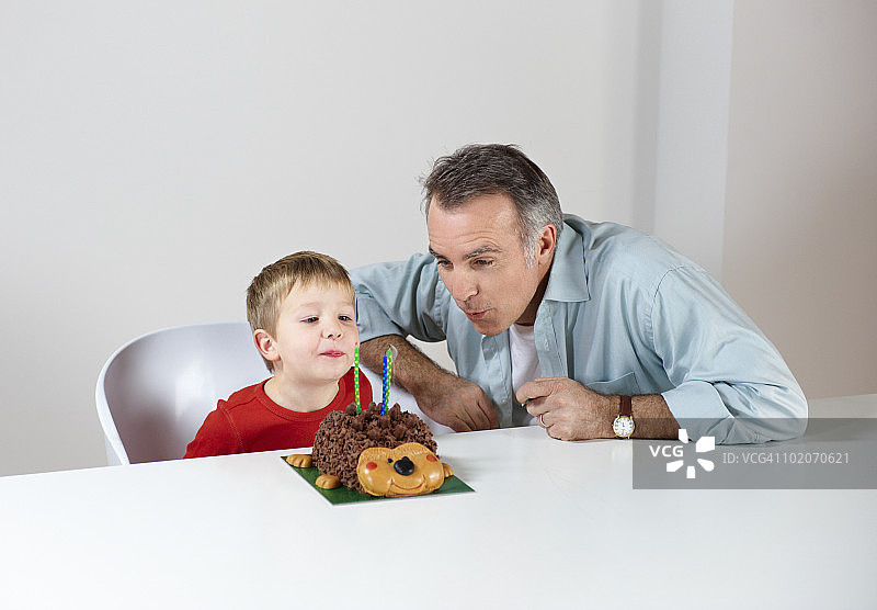 男孩和爸爸一起吹蛋糕上的蜡烛图片素材