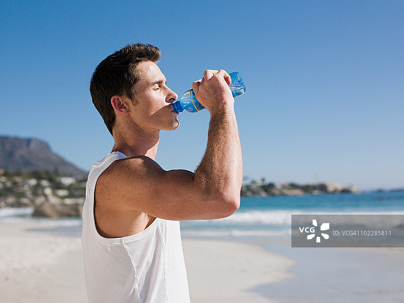 年轻男人在海滩上喝水图片素材