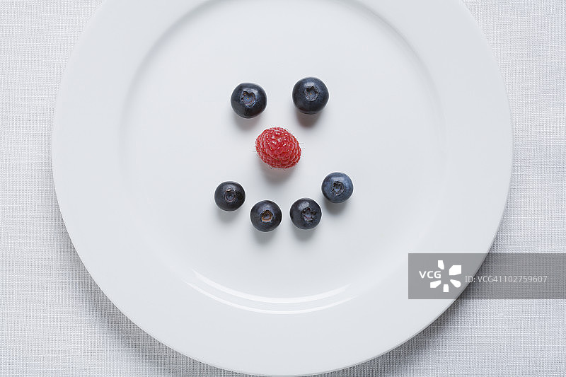 白盘上的蓝莓和覆盆子笑脸图片素材