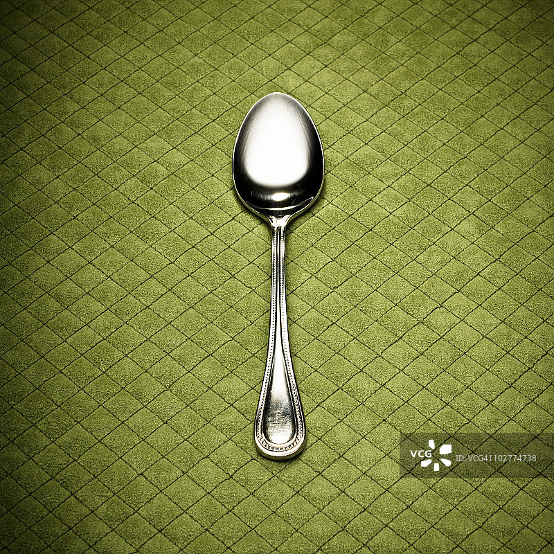 绿色菱形餐垫上的银勺图片素材