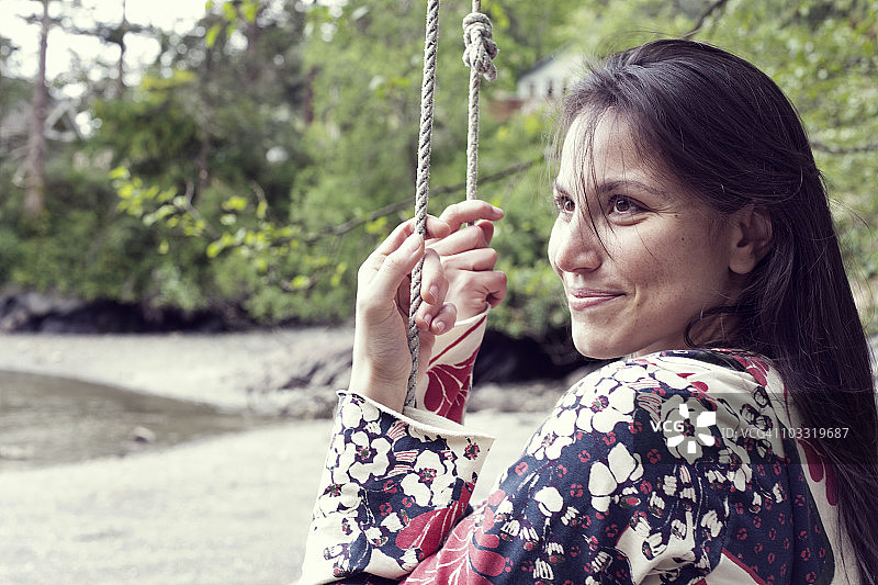 年轻女人在奥卡斯岛猪湾，享受着悬挂在水边树上的秋千图片素材