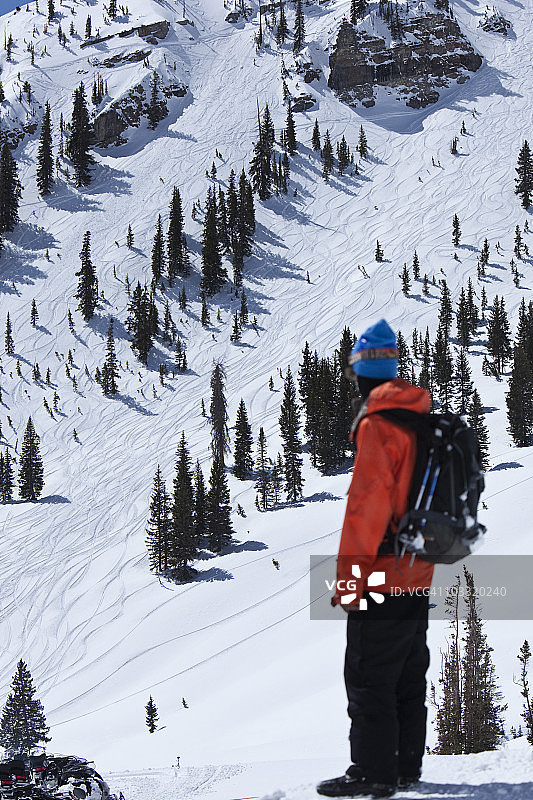 男单板滑雪者回头看着他刚刚在犹他州滑下的巨大悬崖图片素材