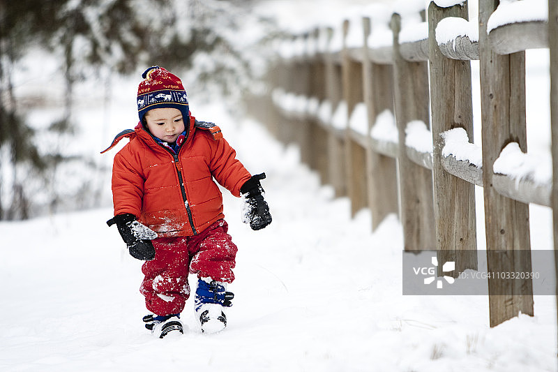 在科林斯堡，一个快两岁的男孩在冬日里走过雪地里的木栅栏图片素材