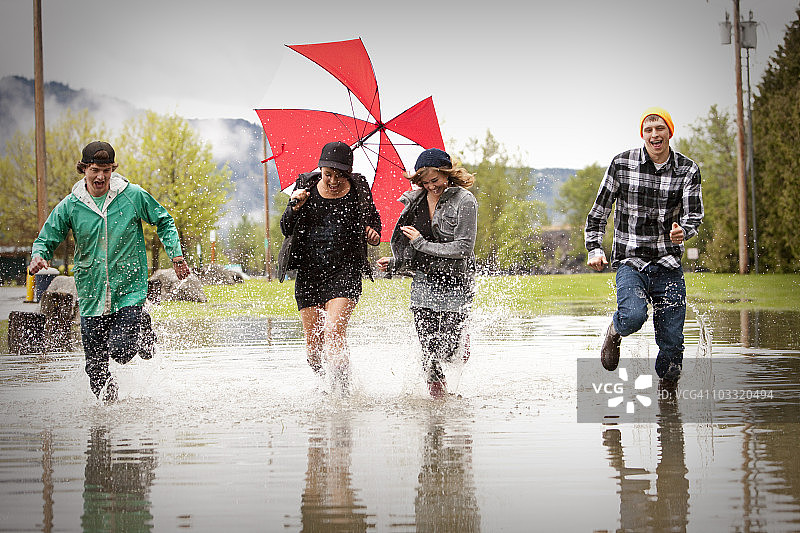 四个年轻人在一个大水坑里奔跑，欢笑图片素材